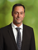 Porträt des Geschäftsführers Karsten Spinner im Anzug vor grünem Hintergrund